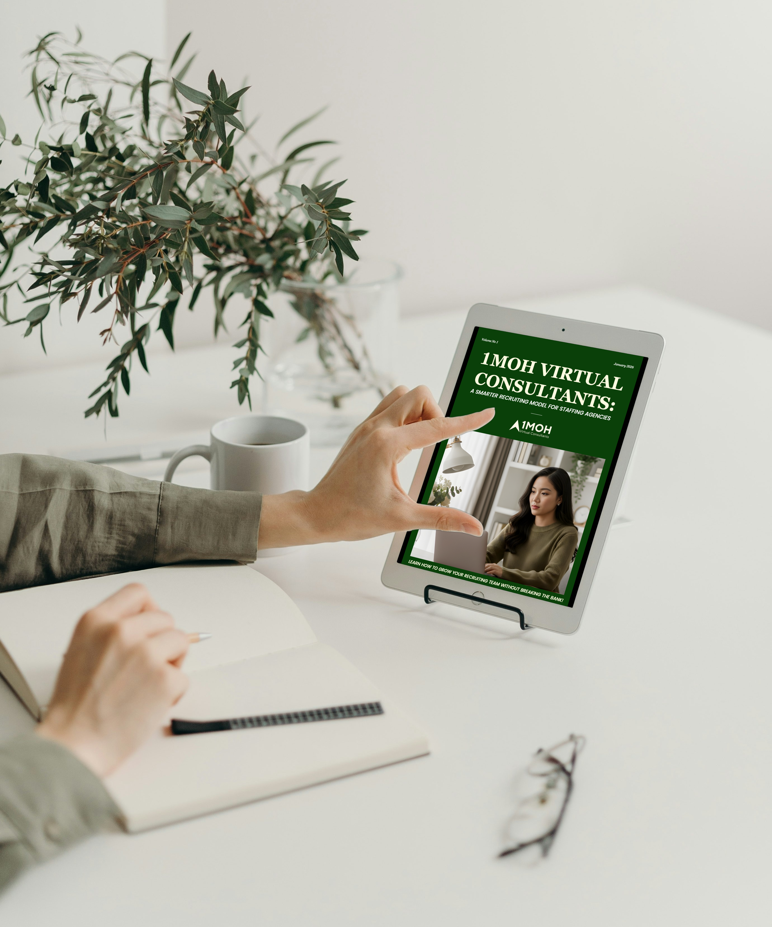 Person using a tablet displaying a flyer titled '1MOH Virtual Consultants: A Smarter Recruiting Model for Staffing Agencies.' on a desk with a notebook, pen, coffee mug, glasses, and a large green leafy plant in the background.
