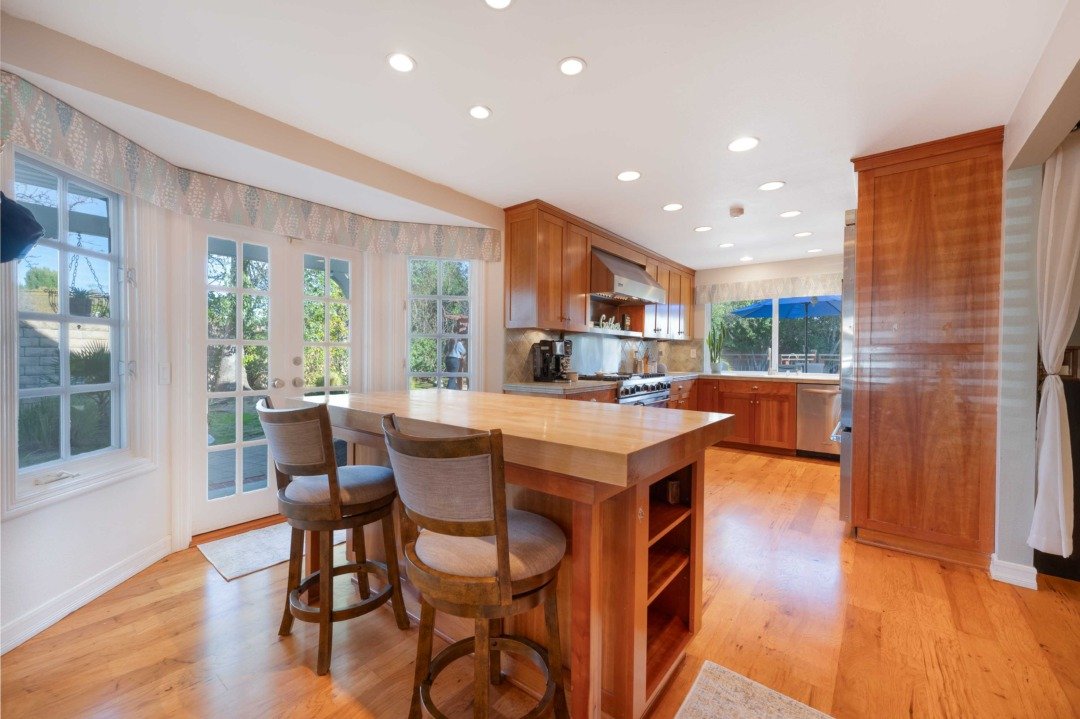 Bright kitchen with wooden cabinets, a large kitchen island, hardwood floors, and multiple windows providing natural light.