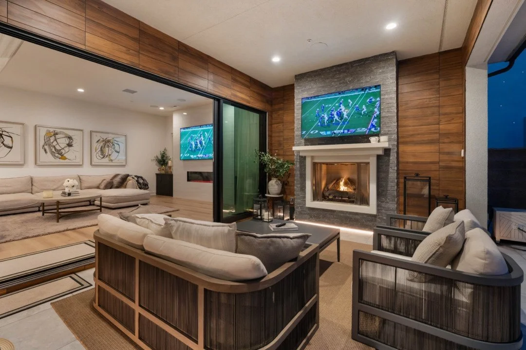 Living room with a fireplace, two televisions showing football, modern furniture, artwork on the walls, and a sliding partition door.