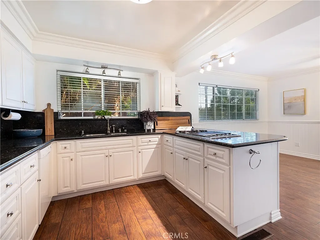 Bright kitchen with white cabinets, black granite countertops, and hardwood floors. Contains a kitchen island with a gas stove, a window above the sink, and modern lighting fixtures.