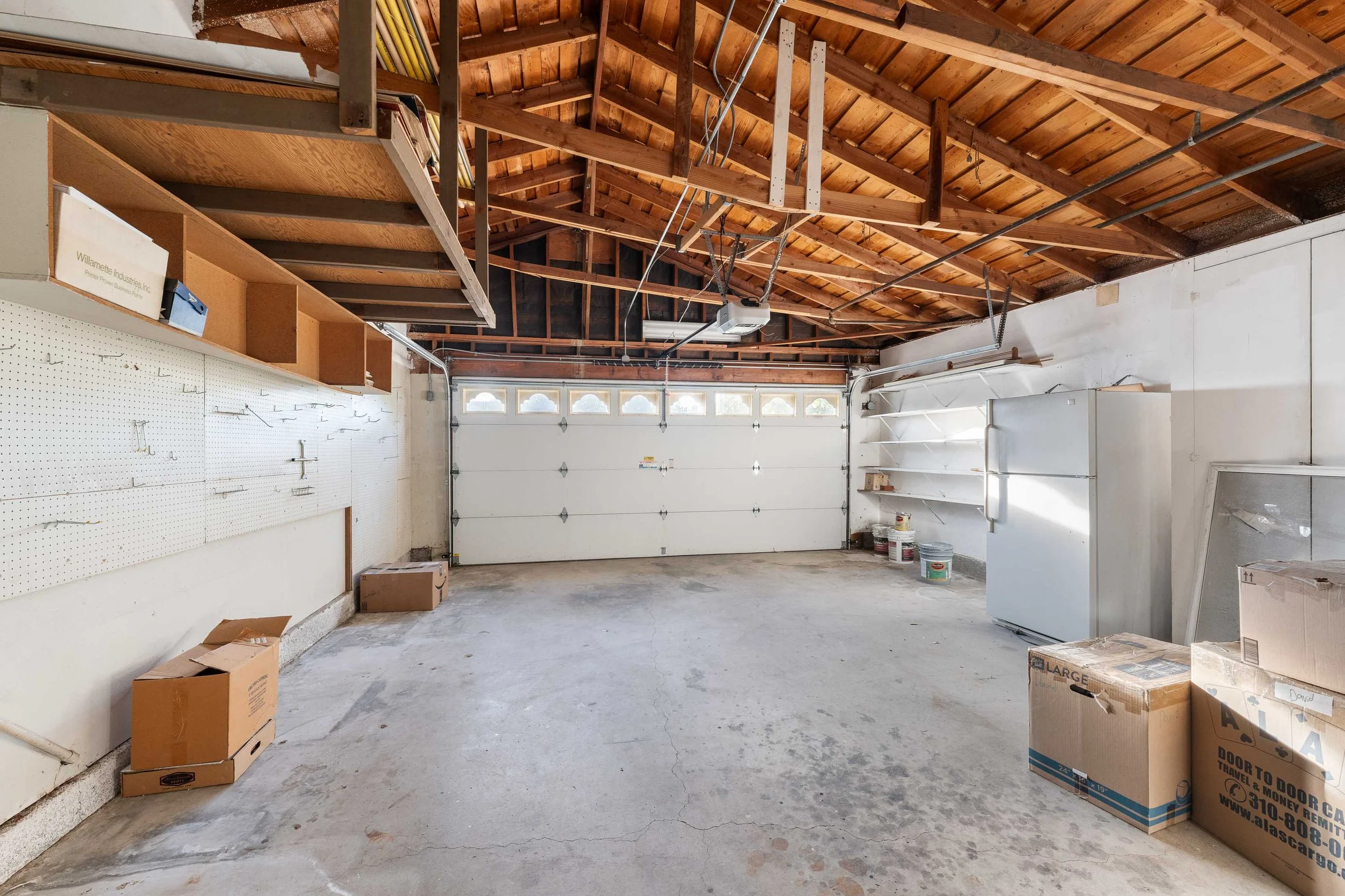 Empty garage with a closed white garage door, wooden shelves, and storage boxes.