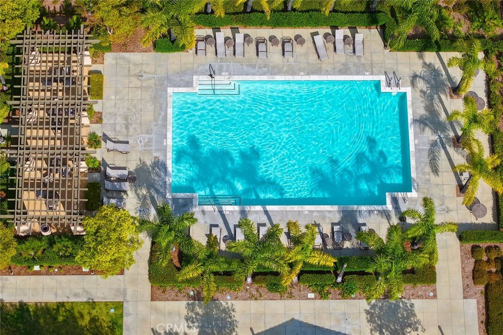 Top-down view of a swimming pool surrounded by lounge chairs, tropical trees, and a patterned pergola in a landscaped backyard.