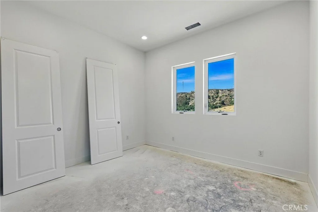 Empty white room with two closed closet doors and two windows showing a landscape with hills and blue sky.