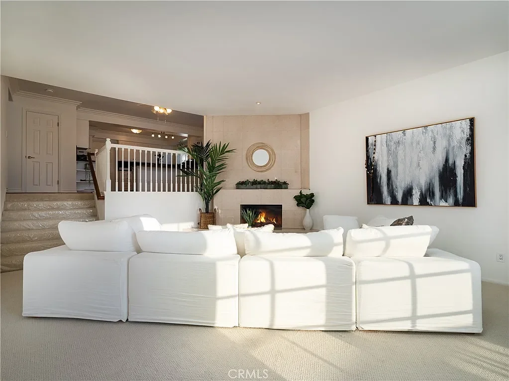Bright living room with a white sectional sofa, a fireplace, a large abstract painting, and natural sunlight streaming through windows.