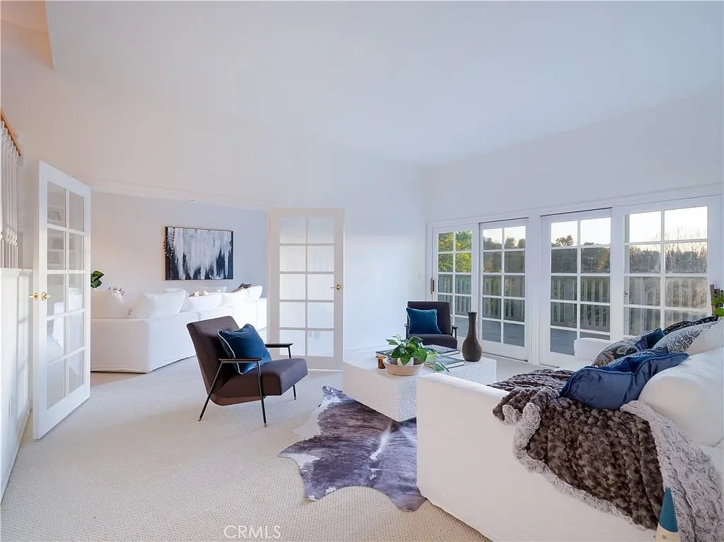 Bright and spacious living room with white sofas, dark armchairs with blue pillows, large windows, and minimal decor.