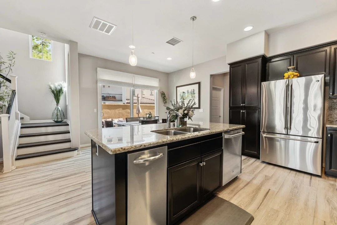 Modern kitchen with black cabinets, stainless steel appliances, granite countertop island, and light-colored hardwood floors.