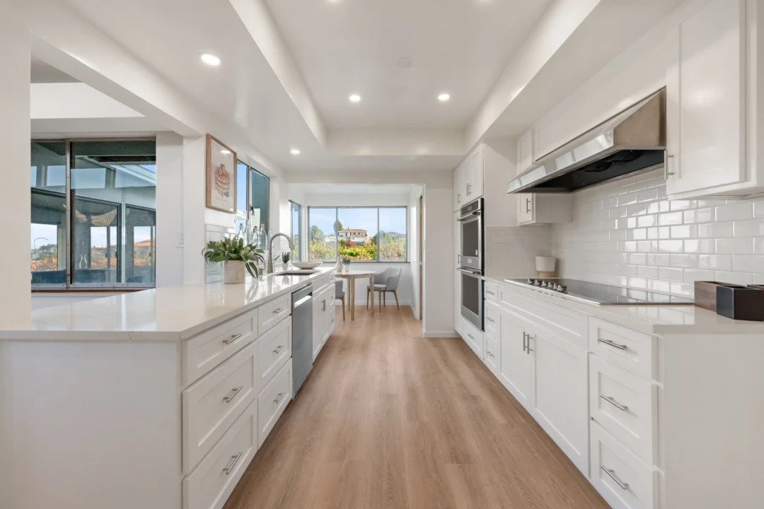 Bright, modern white kitchen with wooden flooring, window view, and minimal decor.