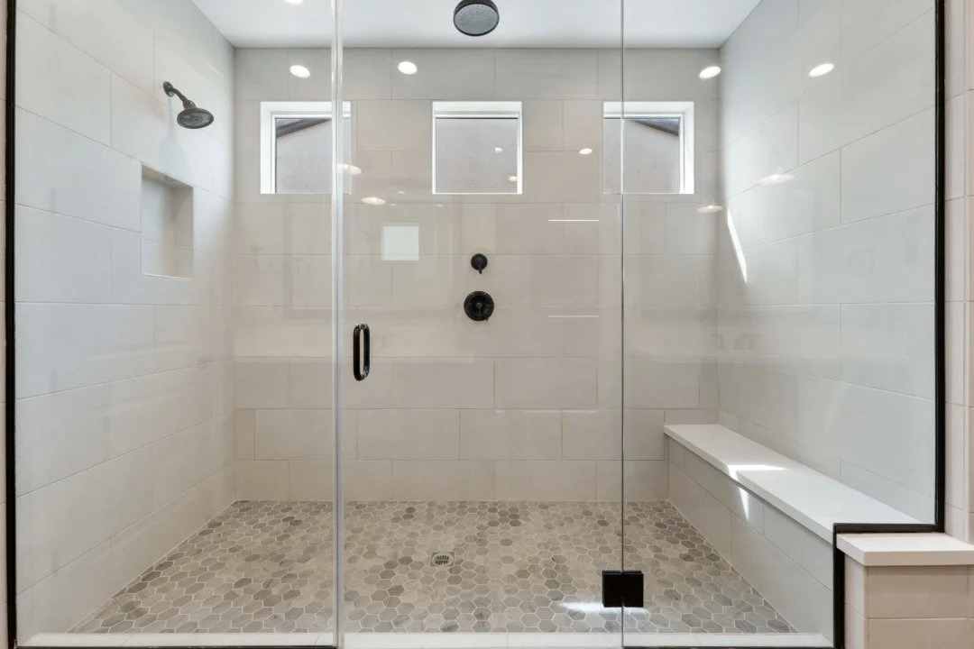 Modern walk-in shower with beige tiled walls, hexagonal floor tiles, a built-in bench, and three small windows at the top, enclosed by a glass door.