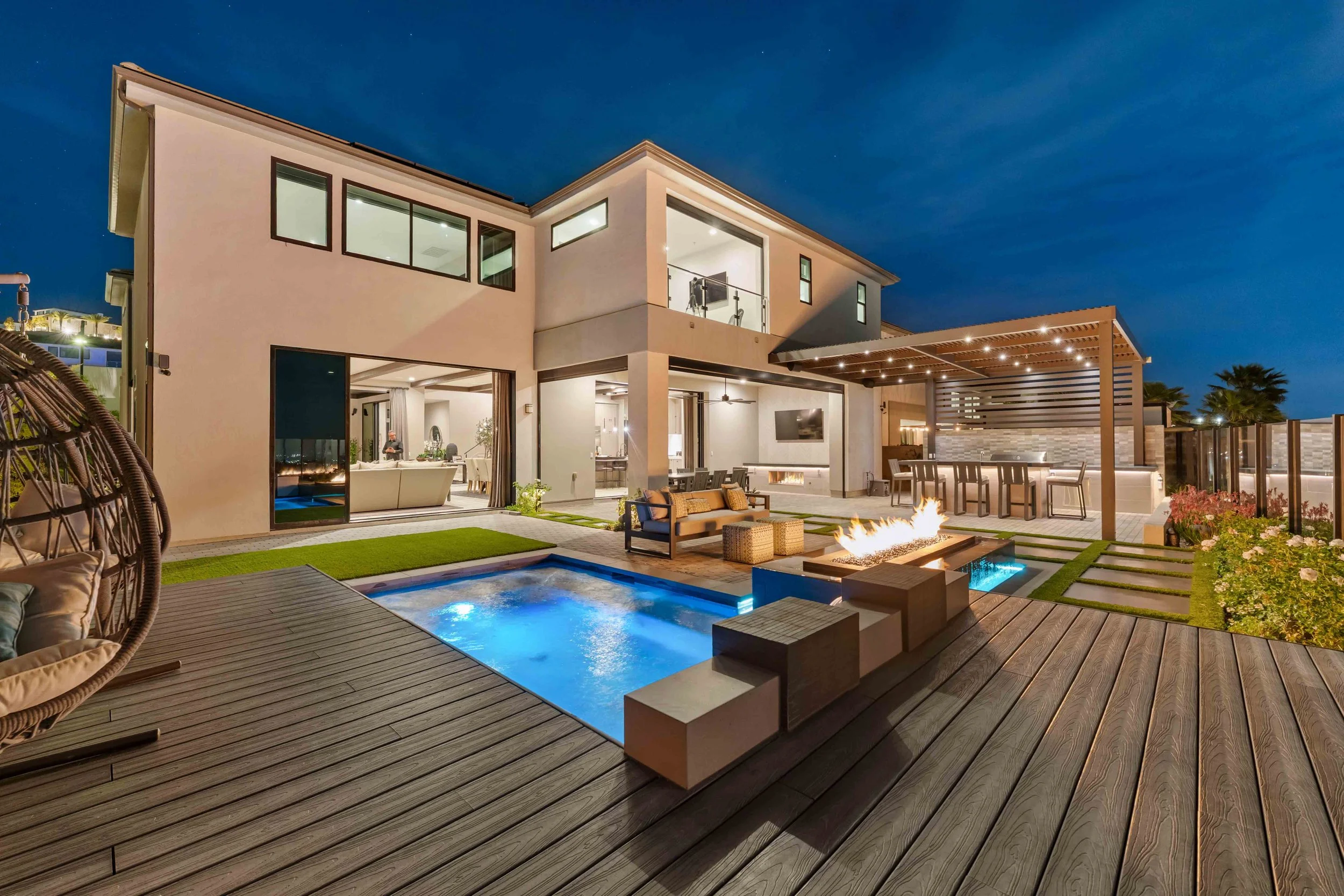 Modern two-story house with outdoor patio, swimming pool, fire feature, and outdoor seating area at night.