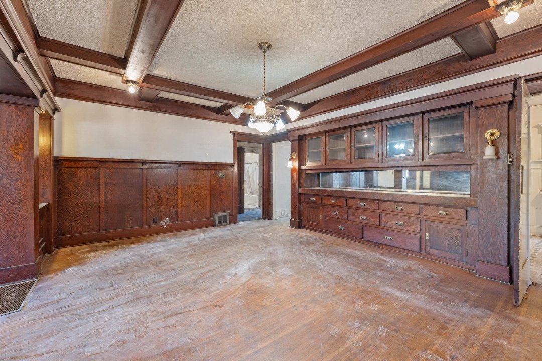 Empty dining room with wooden wall paneling, built-in wooden cabinet, and hardwood floors.