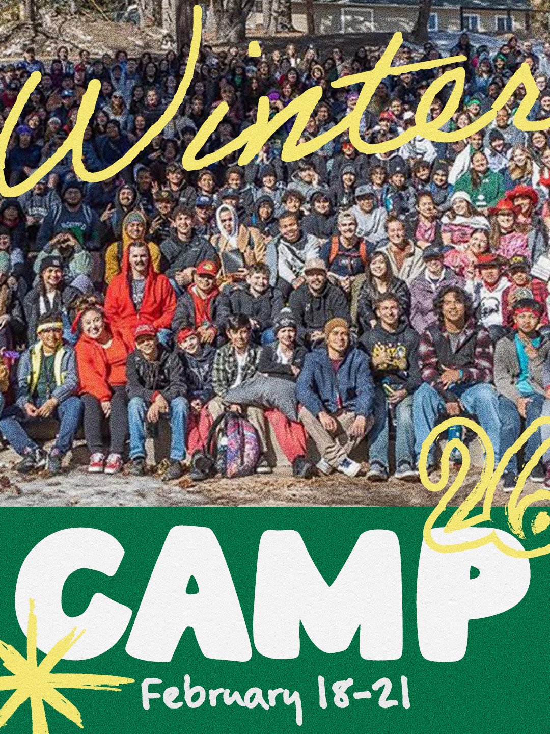 A large group of people, including children and adults, gathered outdoors for a group photo at a camp event, with a sign indicating it is a winter camp from February 18-21.