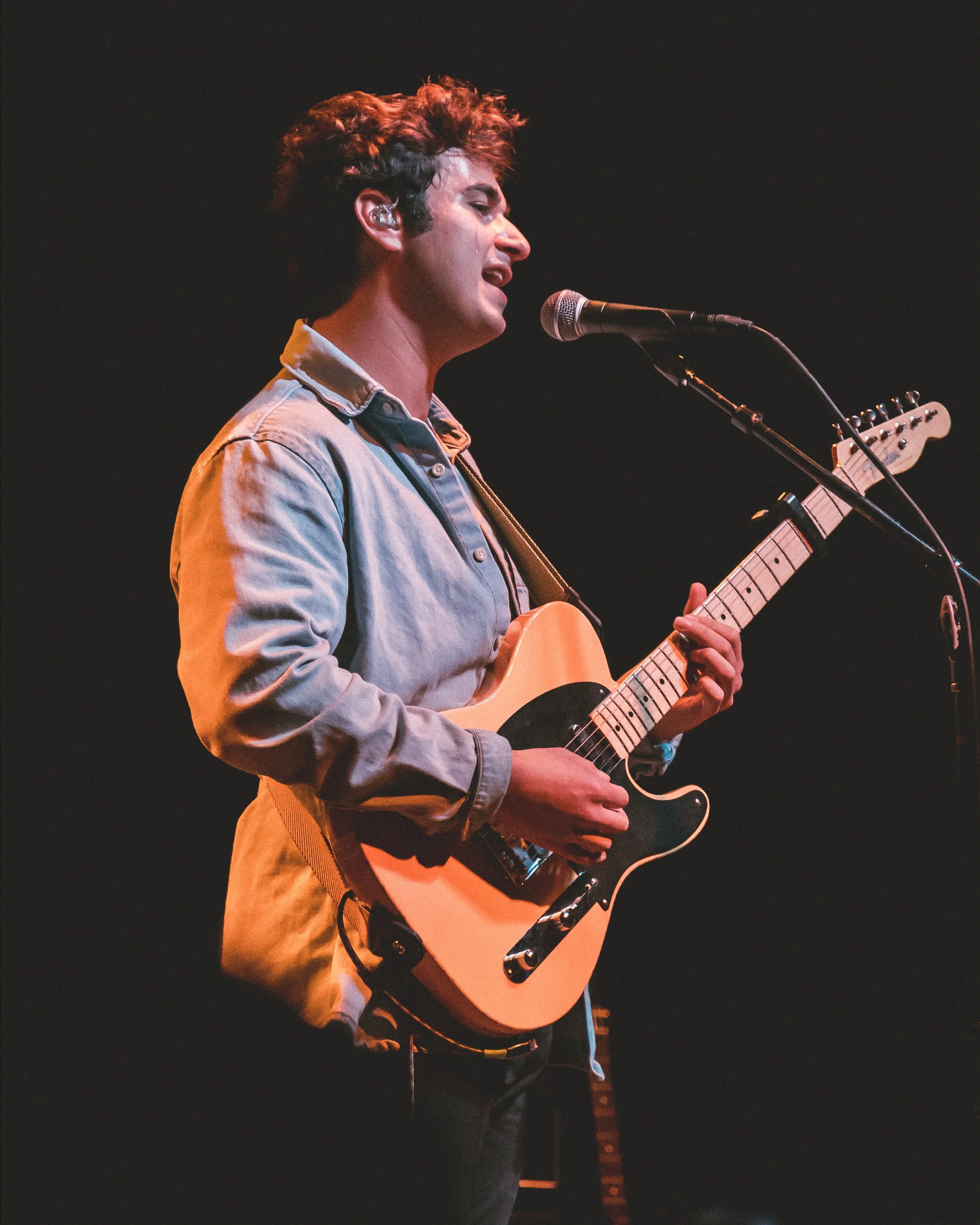 A young man singing into a microphone while playing an electric guitar.
