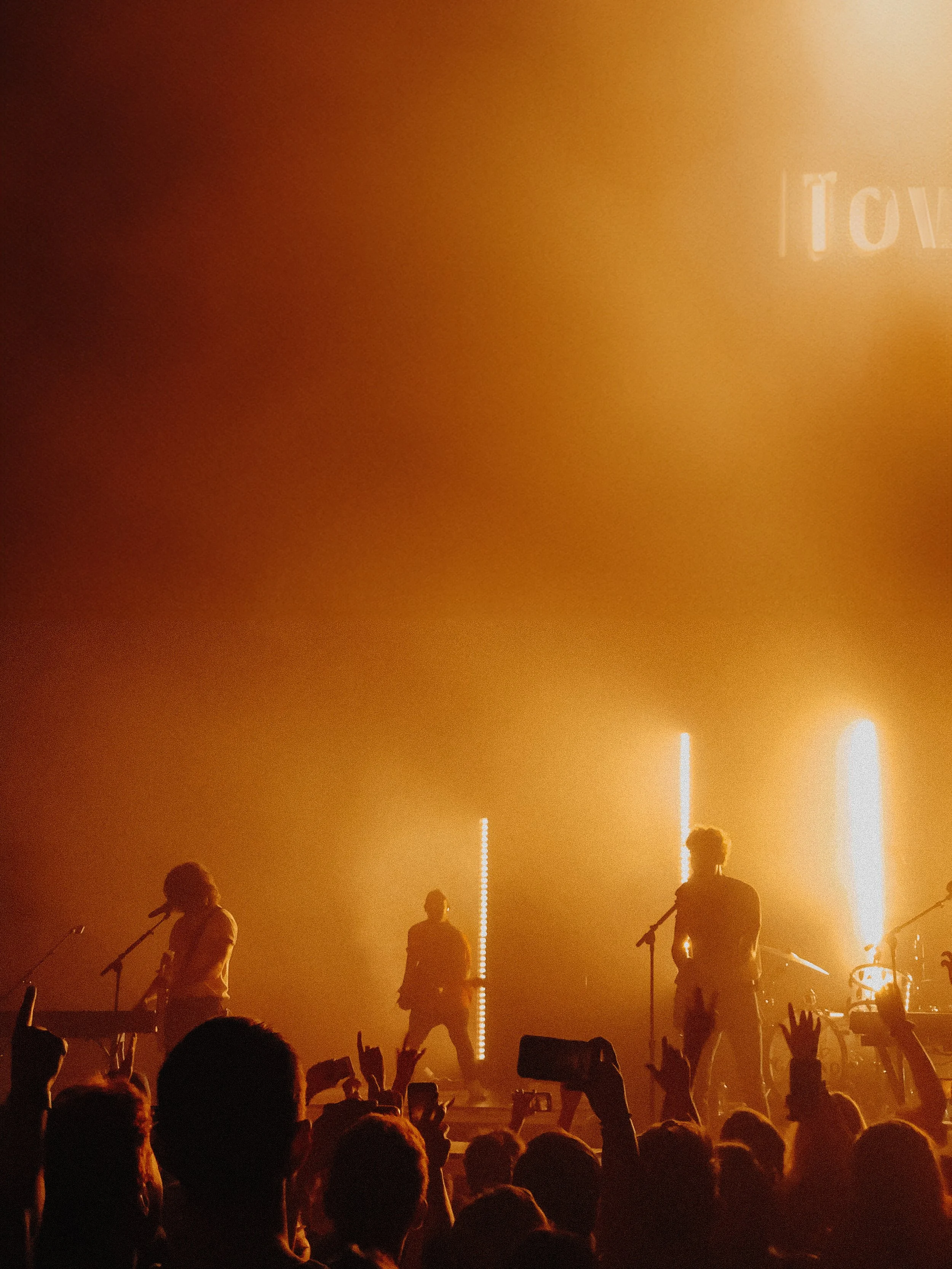Silhouettes of musicians performing on stage with orange lighting and audience in foreground
