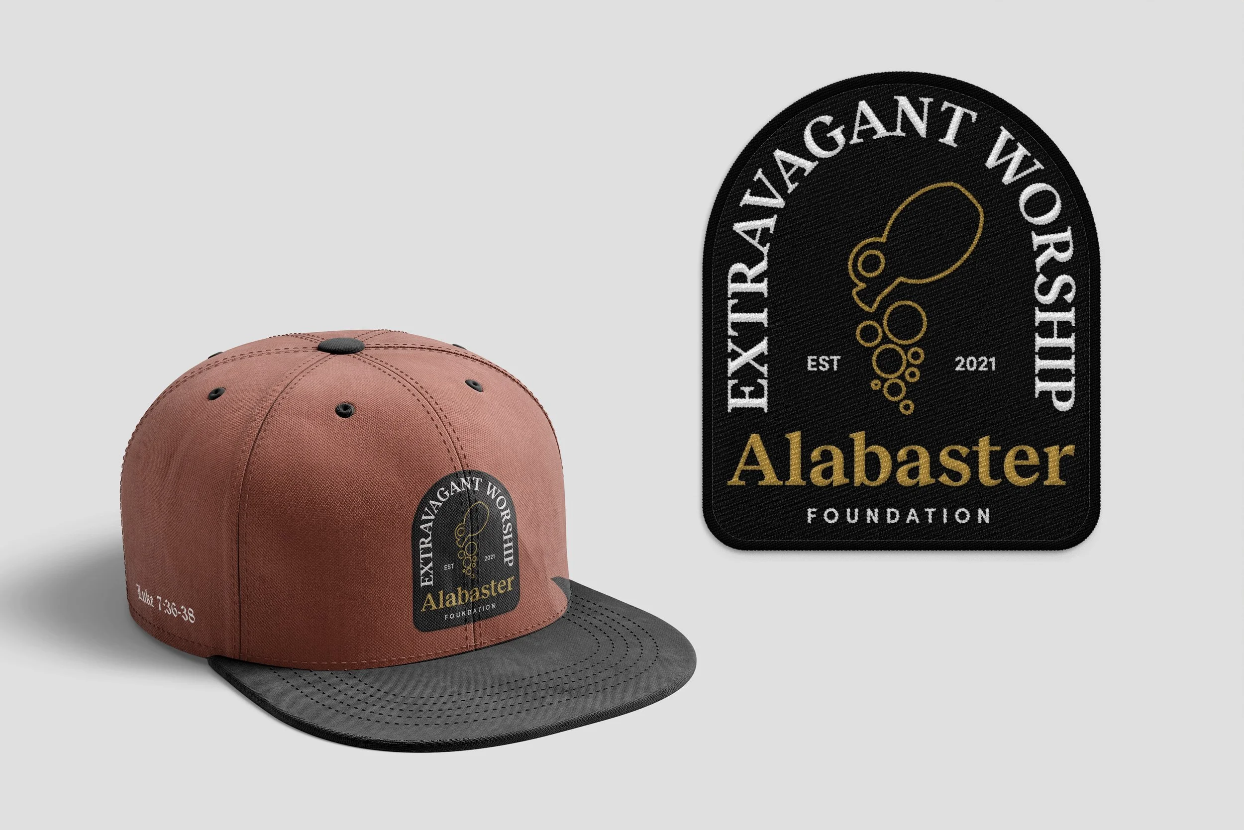A pink baseball cap with a black brim and a patch on the front that reads 'ExtraVAGANT WORSHIP Alabaster Foundation' with a gold logo of a stylized animal, and a matching embroidered patch beside it.