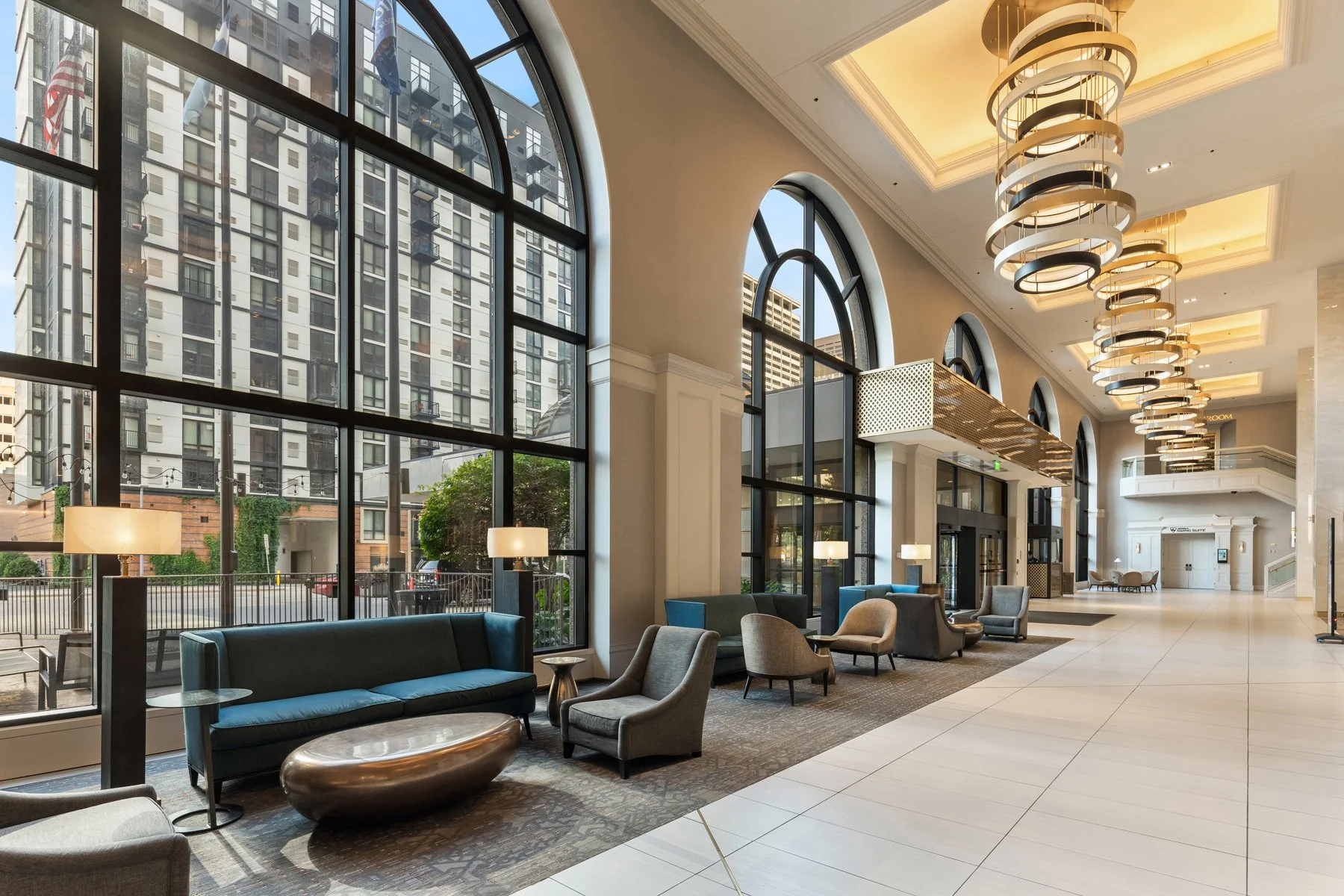 Hotel lobby with large arched windows, modern furniture, and a high ceiling with stylish chandeliers.