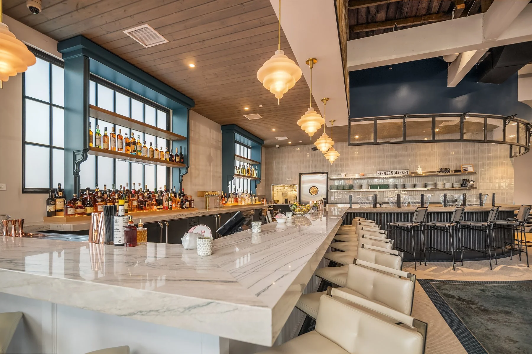 Modern bar with white marble countertop, barstools, and hanging pendant lights.