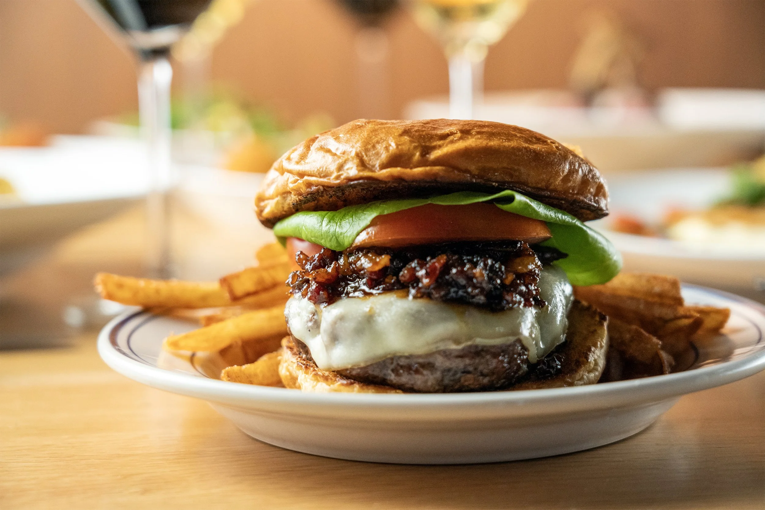 Close-up of a cheeseburger with lettuce, tomato, melted cheese, barbecue sauce, and a beef patty, served with French fries on a plate.