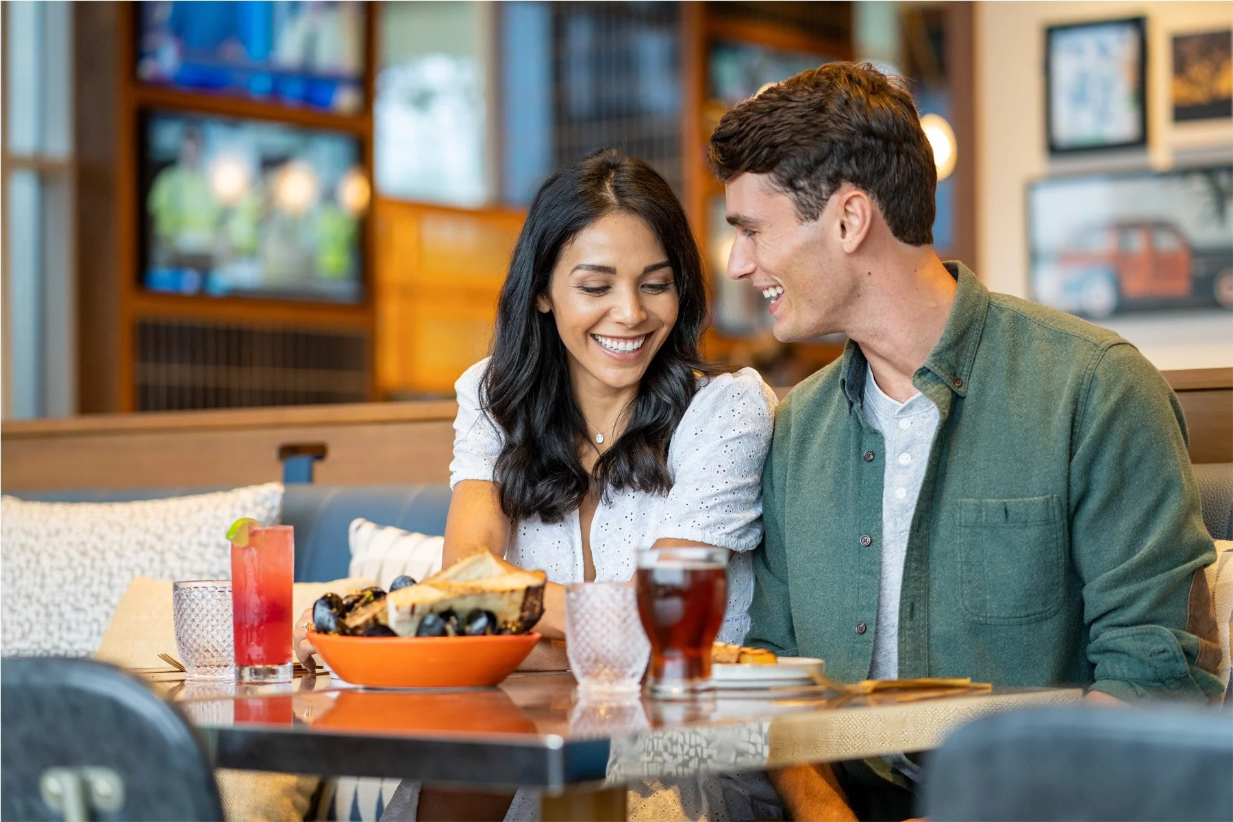 A smiling couple sitting at a restaurant table sharing a meal and drinks.