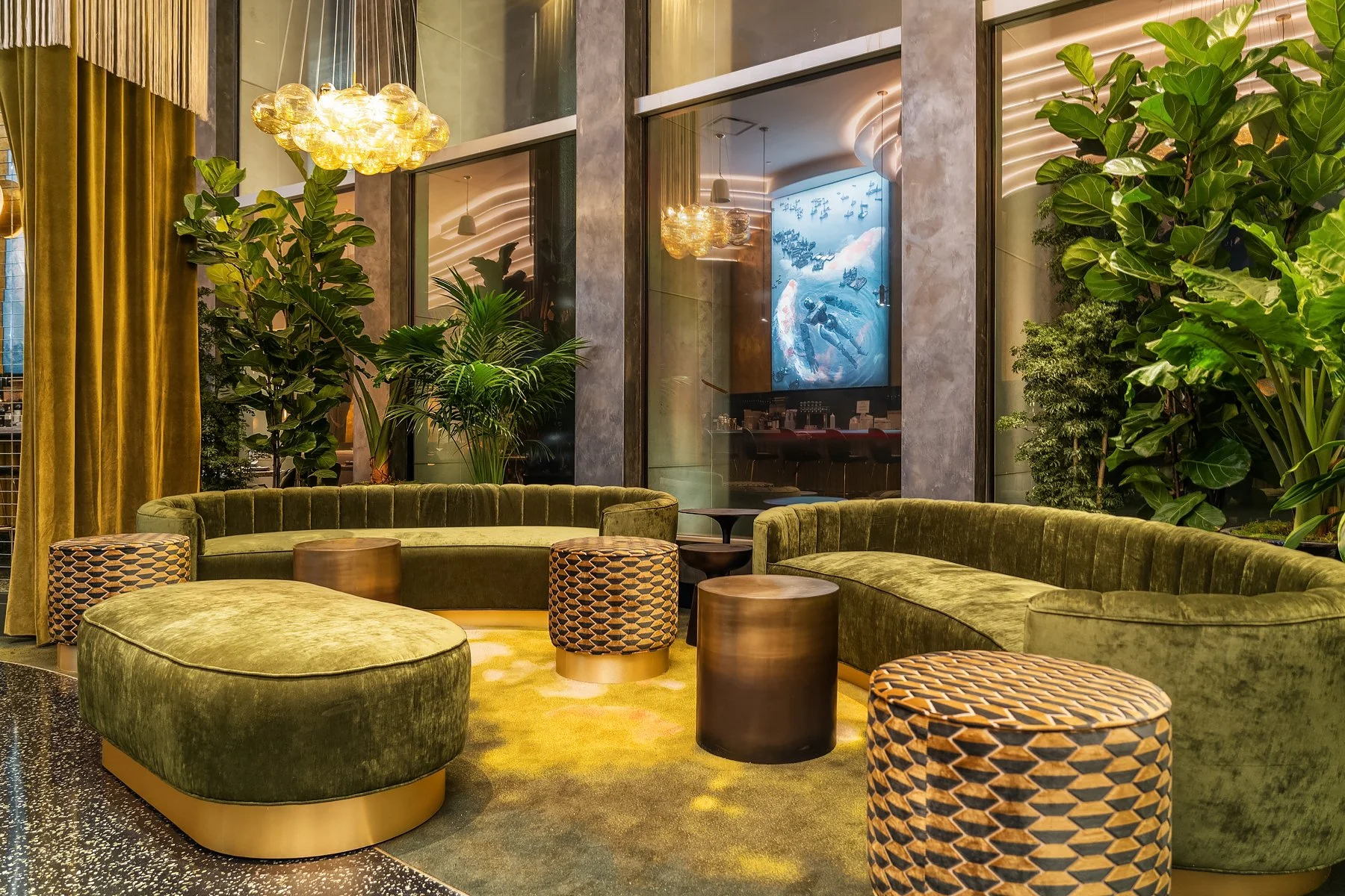 Restaurant lounge with green velvet sofas, patterned ottomans, plants, and modern decor.