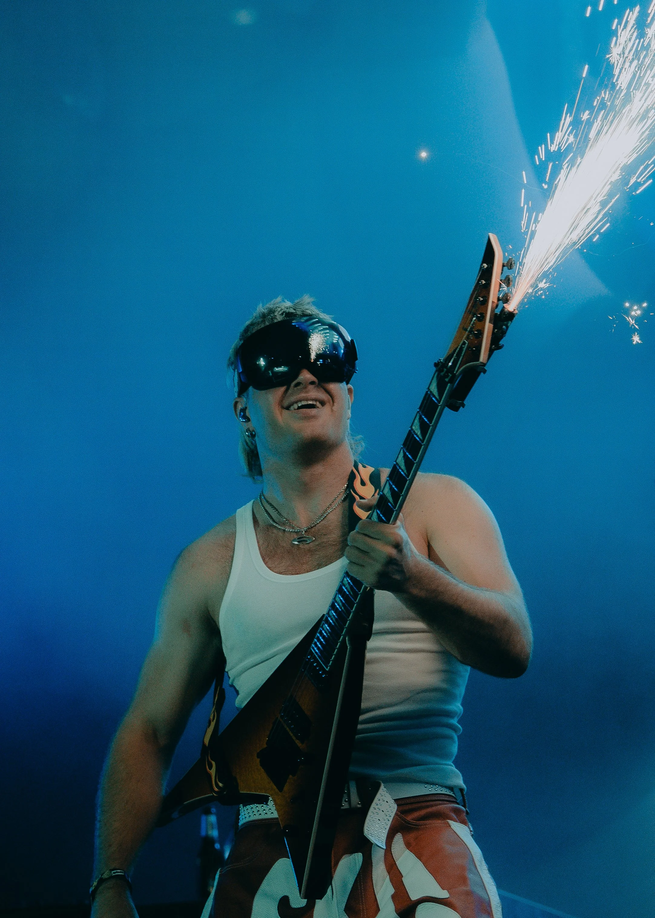 Person wearing sunglasses, holding a guitar, with fireworks in the background during a celebration.