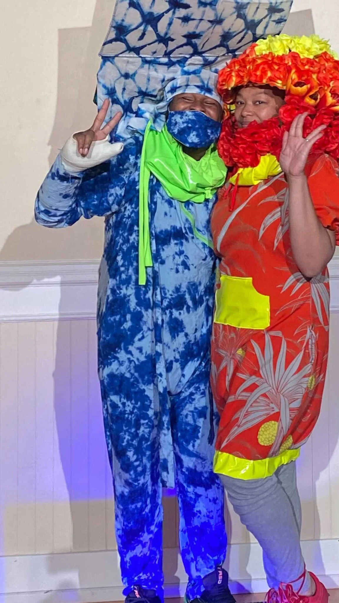 Afatasi the Artist poses in her elaborate red and yellow garment along with a model wearing blue and white patterened onesie with a matching sculpture extending from their back.
