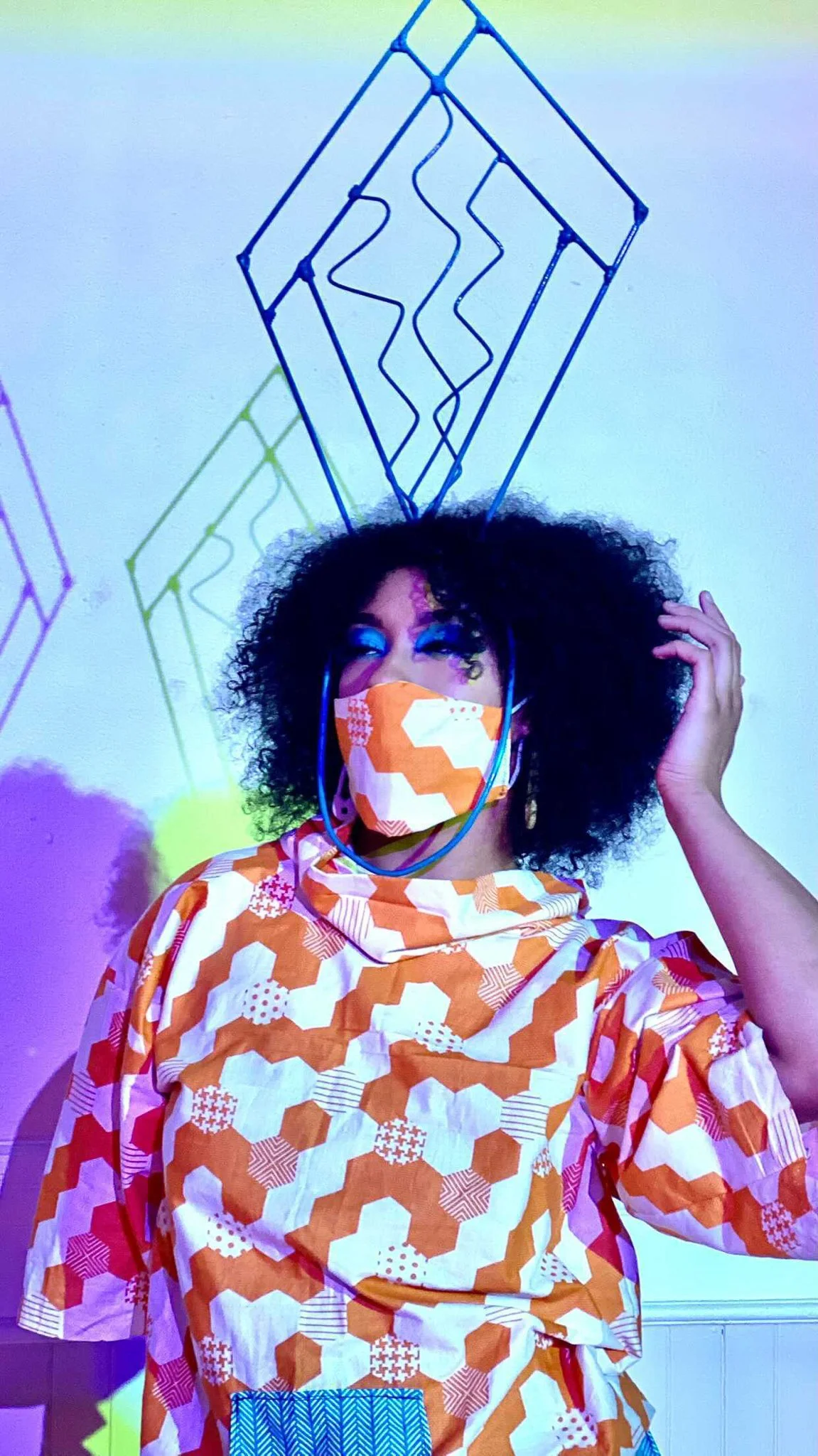 Closeup of Black, female model wearing an orange patterned mask with matching top 