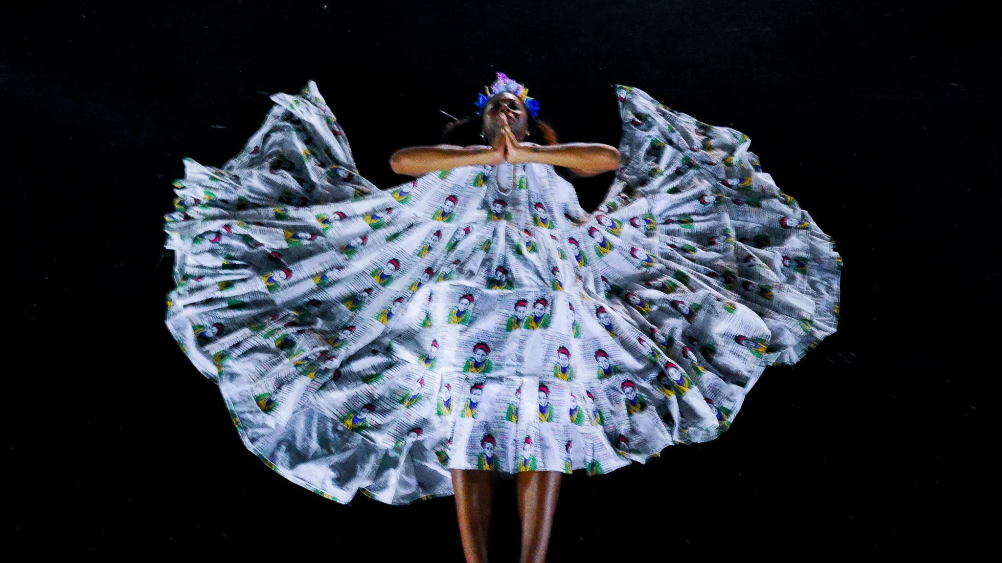 A black, female  model in  flowing sliver garment that extends in all directions around her giving her an angelic presence.