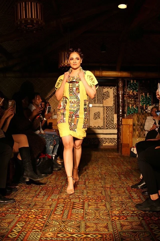 A model walks the runway wearing a short, yellow sack-style dress.