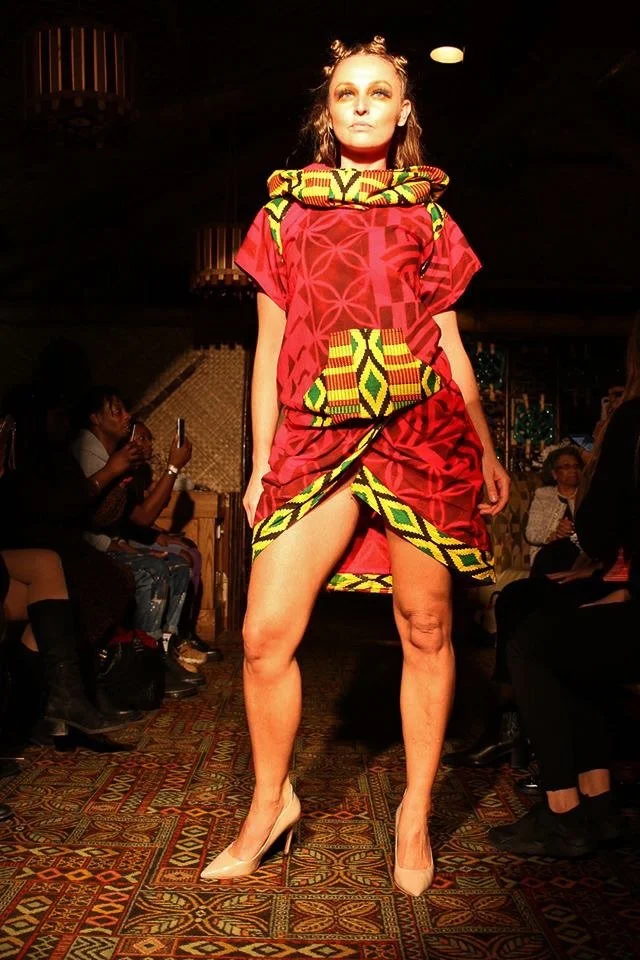 A model poses on the runway wearing a bright red dress with yellow and green detailing