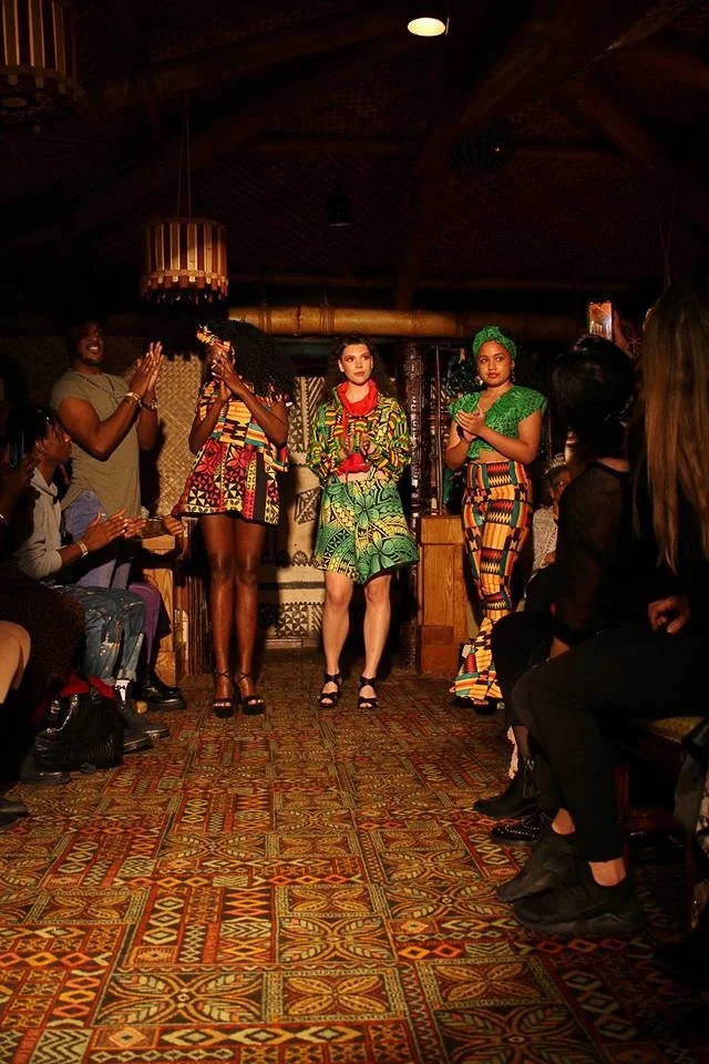 A group of three models stand together in colorful garments. 