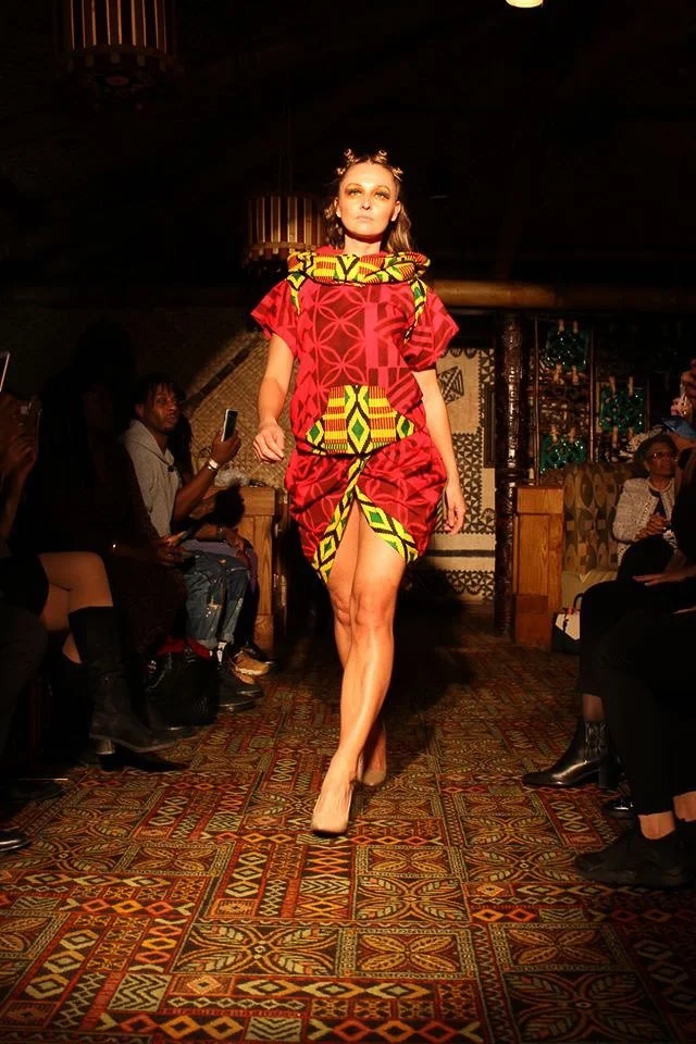 A model walks the runway wearing a bright red dress with yellow and green detailing