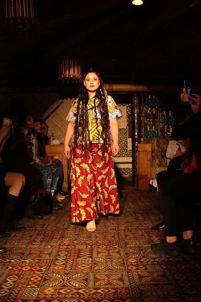 A model walks the runway wearing a flowing red and yellow patterned skirt with a yellow and white patterned top.