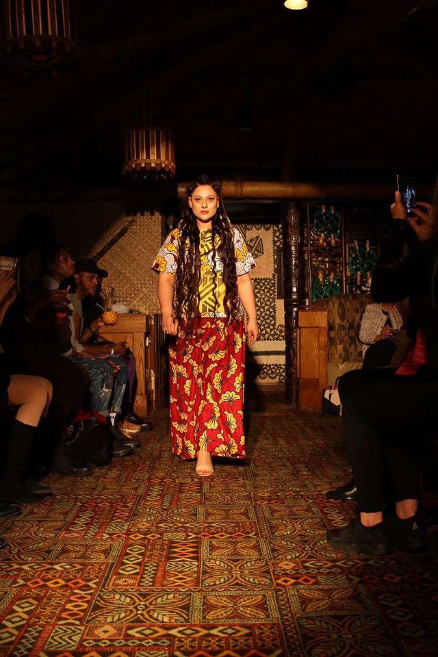 A model walks the runway wearing a flowing red and yellow patterned skirt with a yellow and white patterned top.