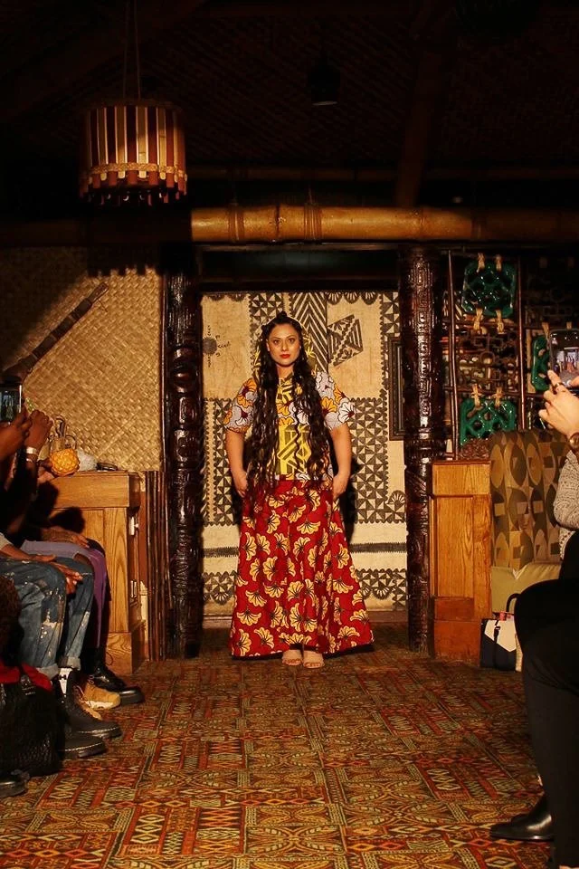 A model enters the runway wearing a flowing red and yellow patterned skirt with a yellow and white patterned top.