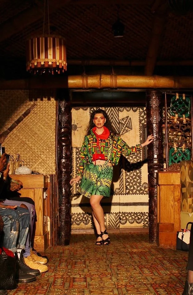A model enters the runway wearing a green and yellow patterned skirt with matching top. A red color frames her neck.
