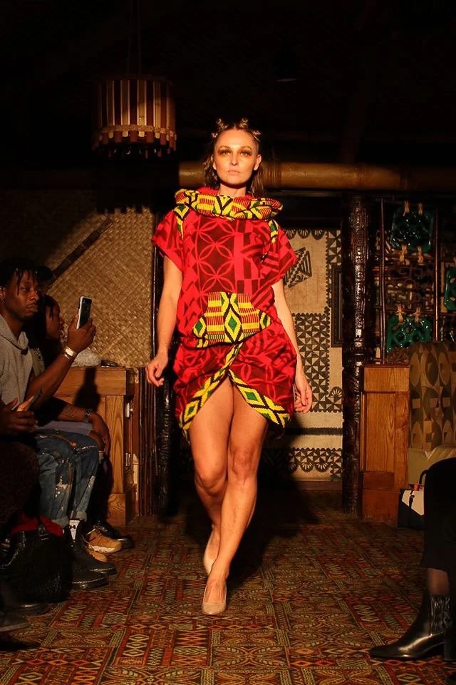 A model walks the runway wearing a bright red dress with yellow and green detailing