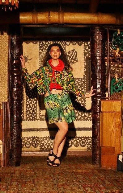 A model enters the runway wearing a green and yellow patterned skirt with matching top. A red color frames her neck.