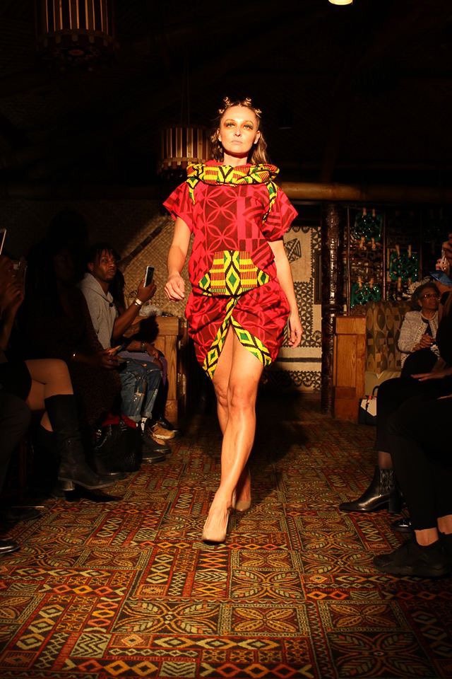 A model walks the runway wearing a bright red dress with yellow and green detailing
