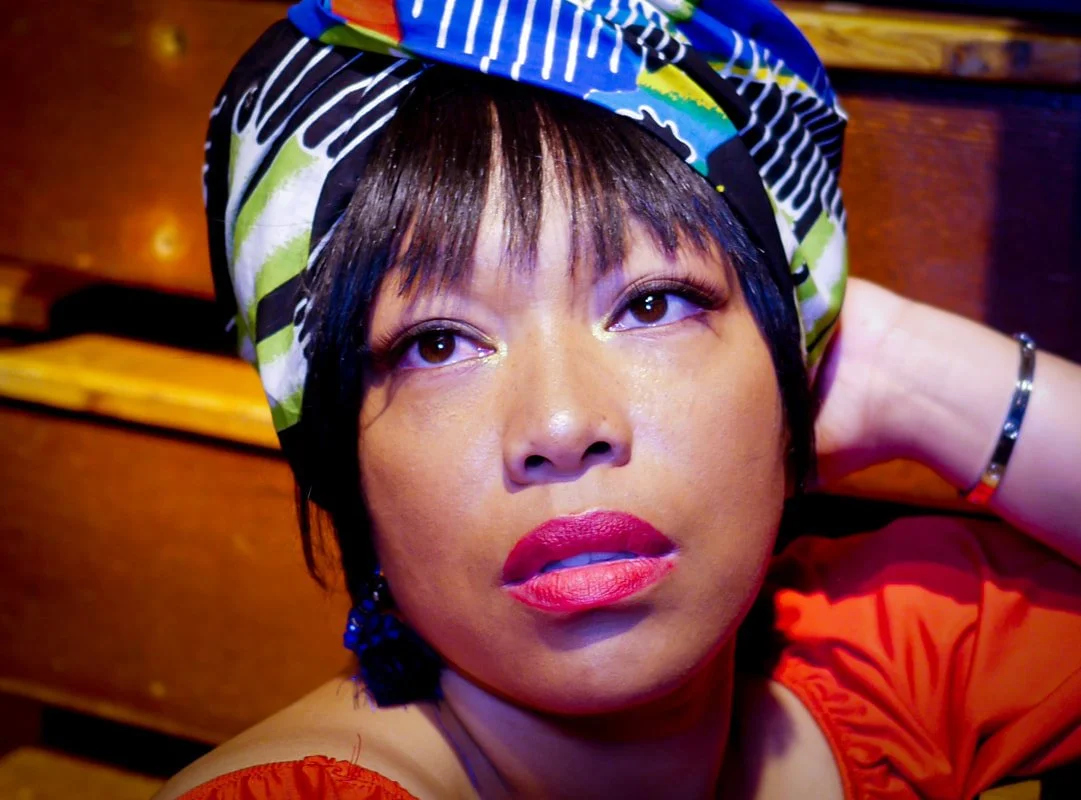A portrait of Afatasi the Artist wearing a colorful head wrap and pink lipstick.