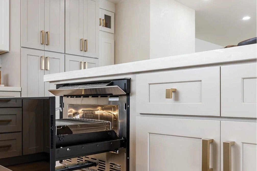 Empty built-in oven in modern white kitchen with gold handles.