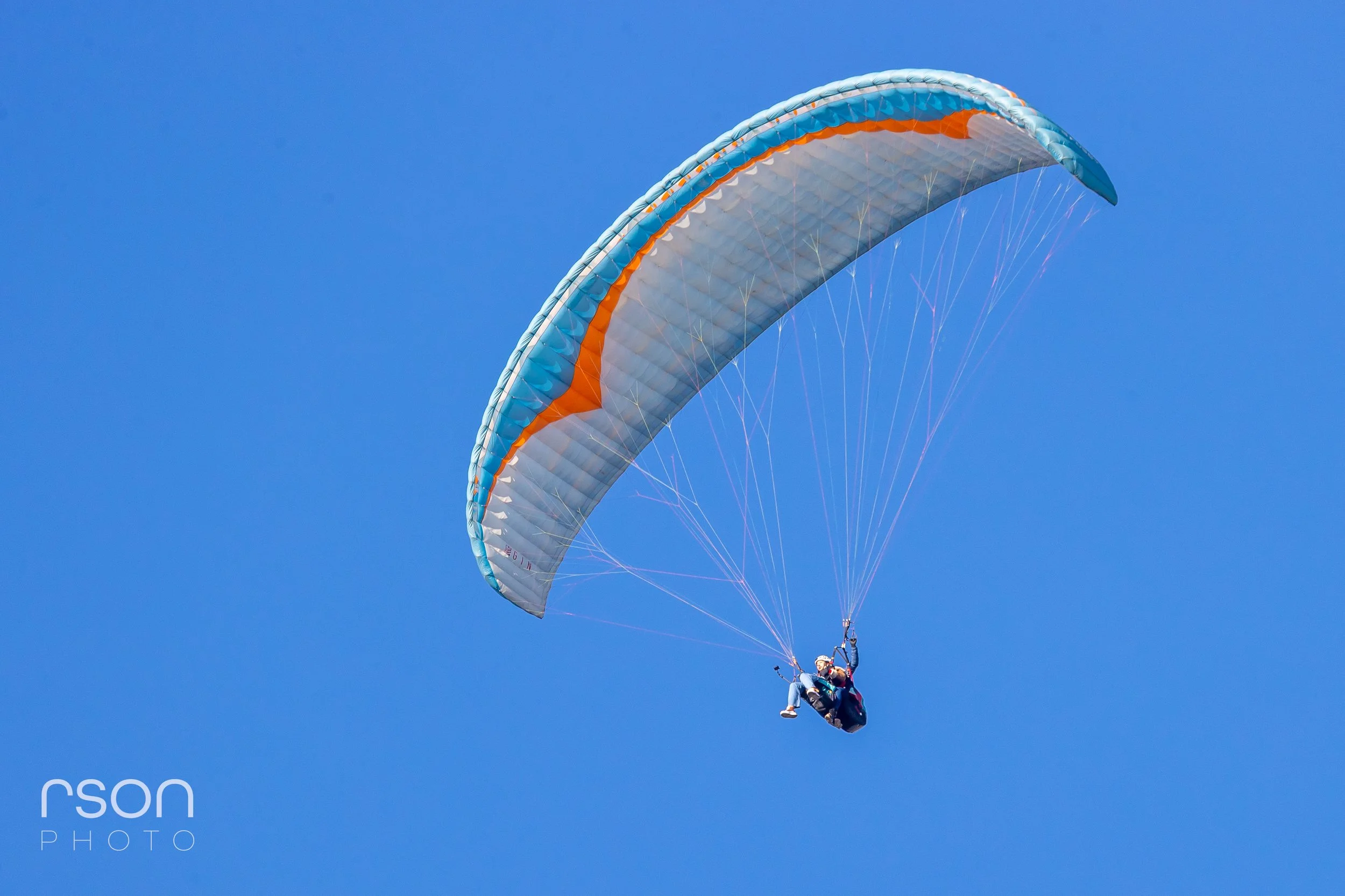 Paraglider flying in clear blue sky.