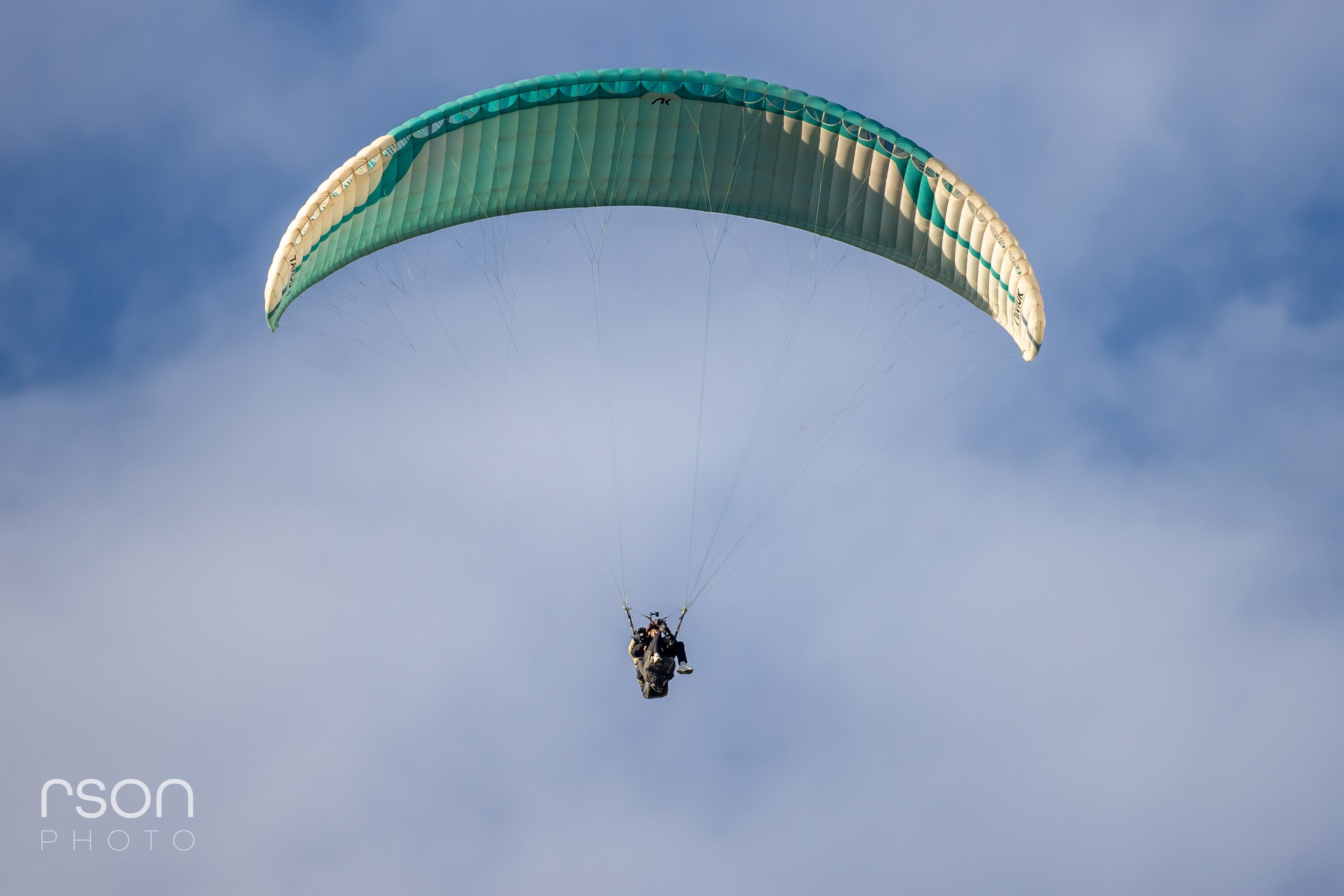 A person paragliding in the sky with a blue and white parachute.