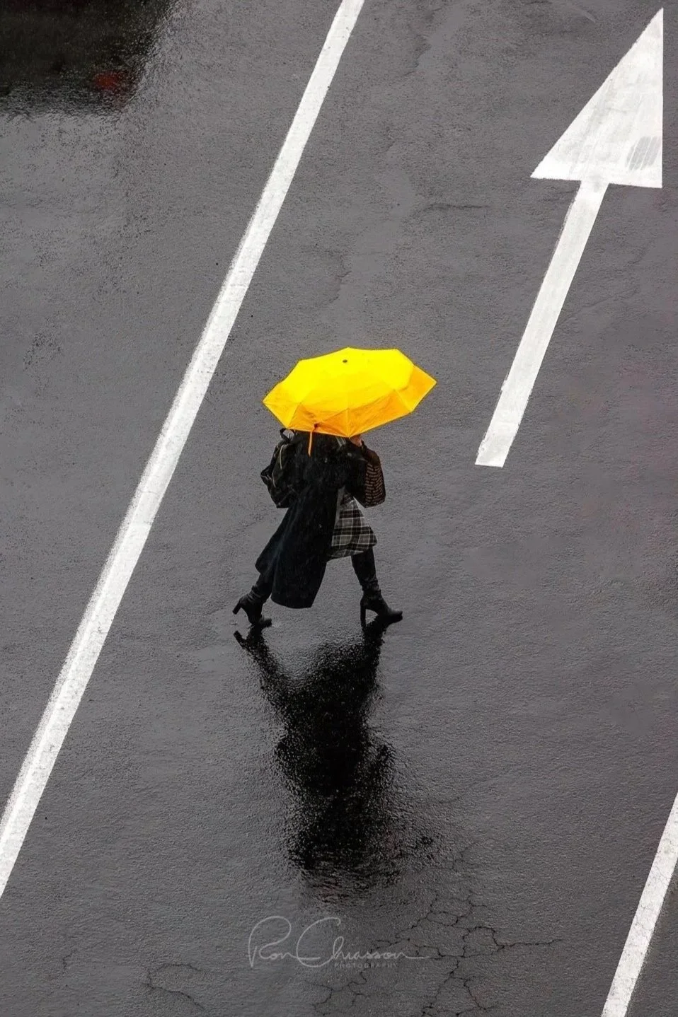 A lady with a bright yellow umbrella crosses the street in the rain. ©Ron Chiasson Photography @rsonphoto.