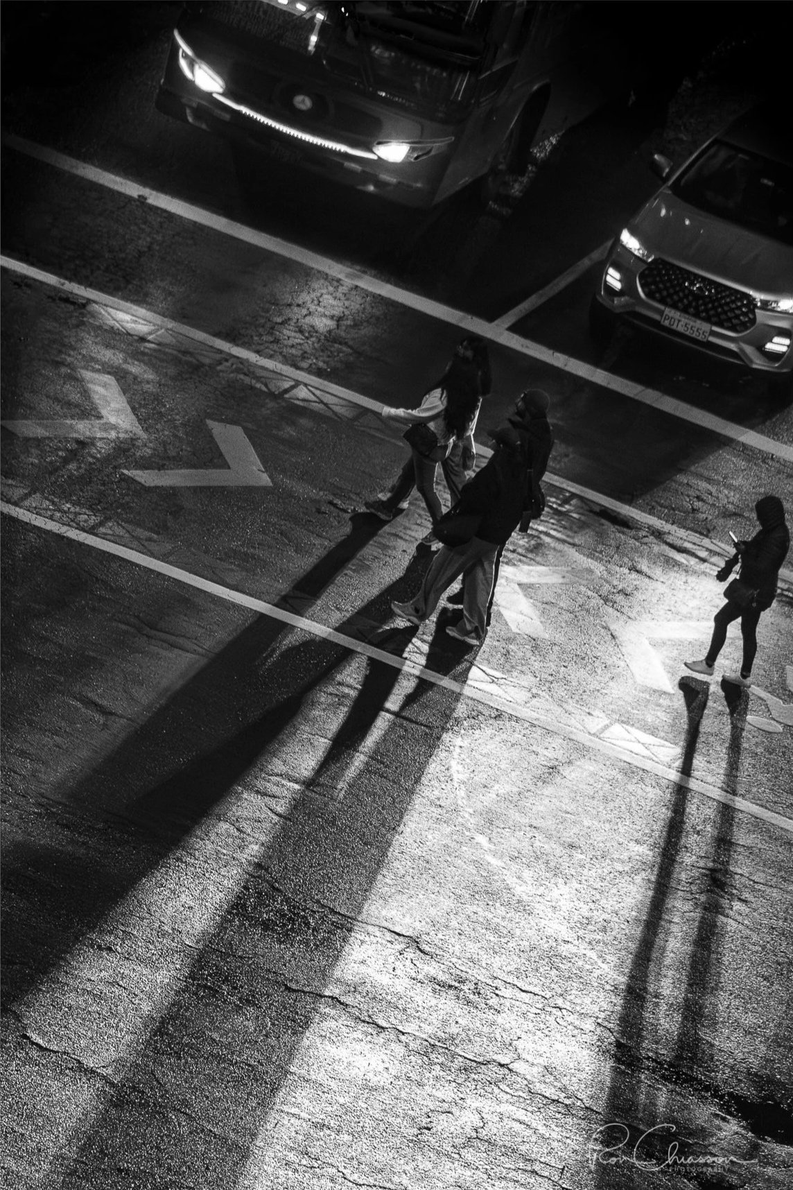 People crossing the road at night with the headlights of cars projecting long shadows. ©Ron Chiasson Photography @rsonphoto.