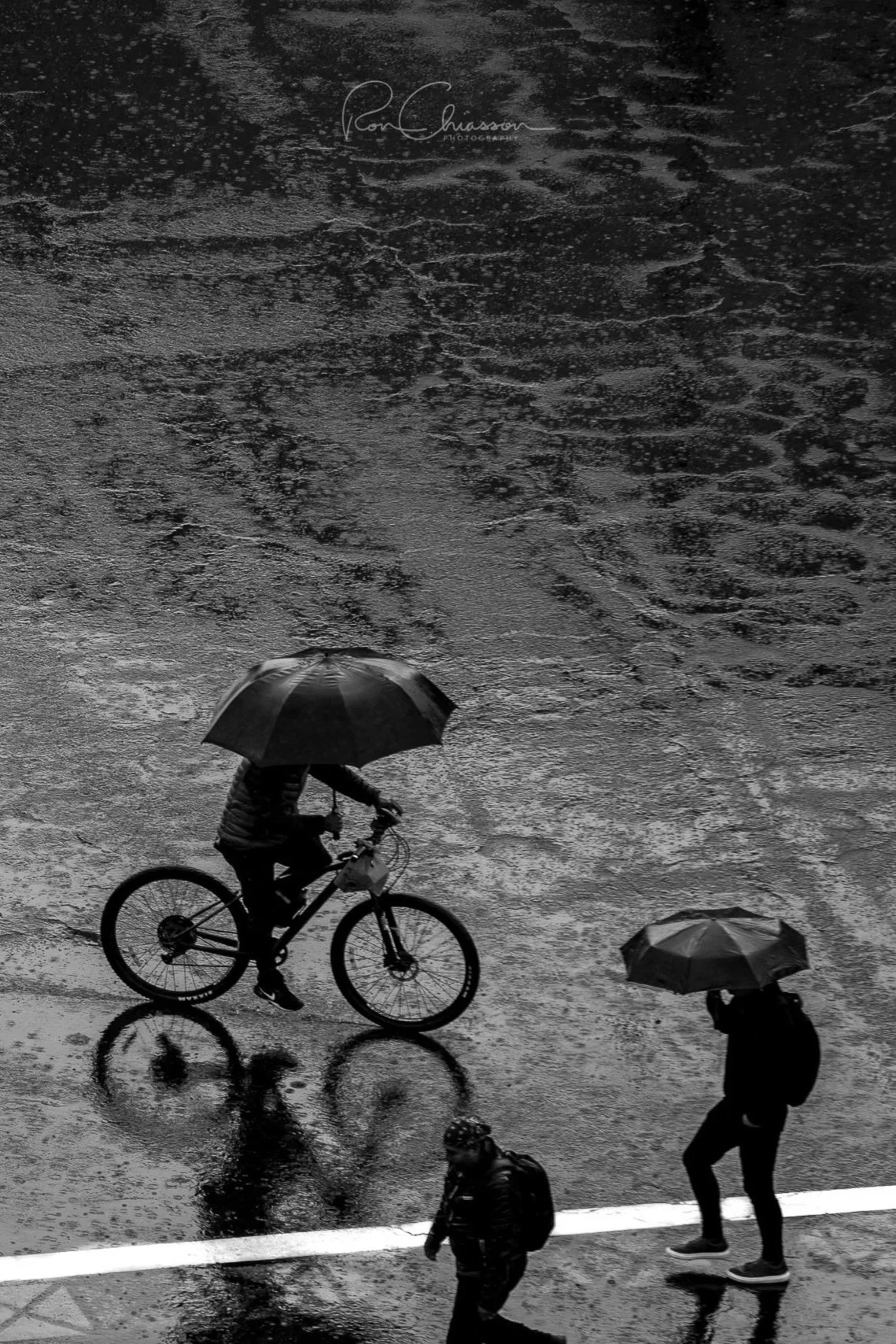 A cyclist with an umbrella crosses the street in the heavy rain. ©Ron Chiasson Photography @rsonphoto.