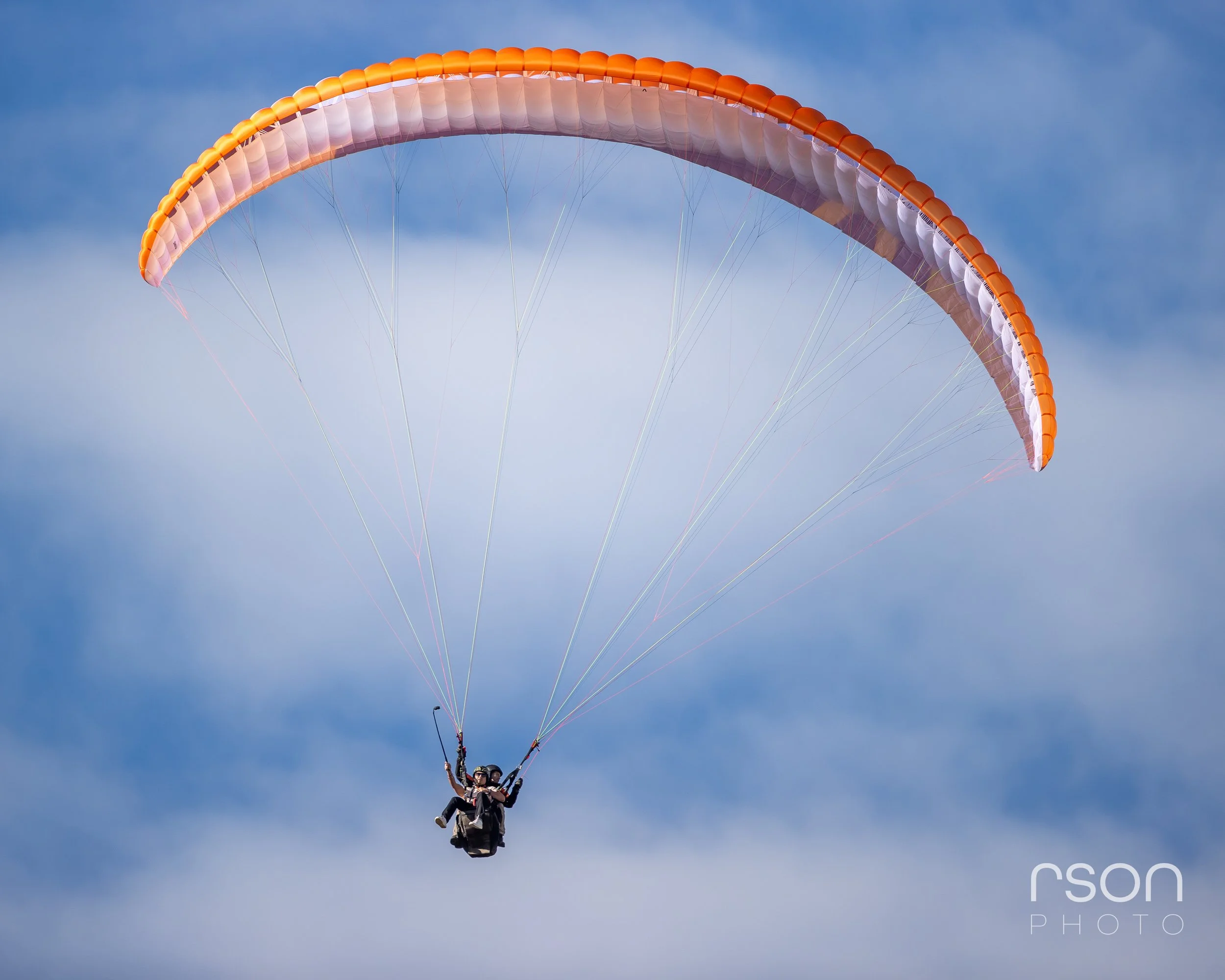 Paraglider flying in a blue sky with scattered clouds