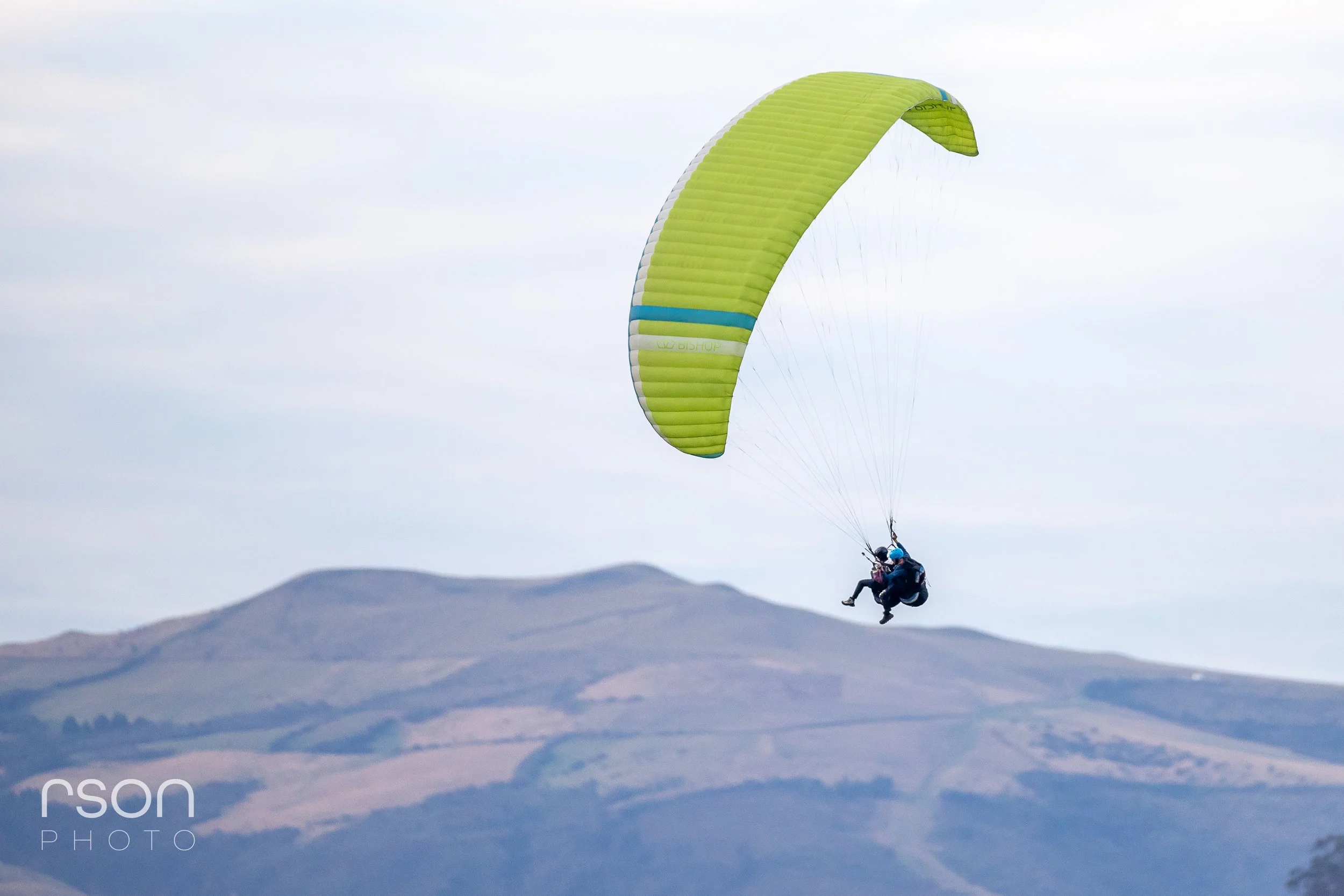 Paraglider flying in the sky above mountains with a lime green canopy.
