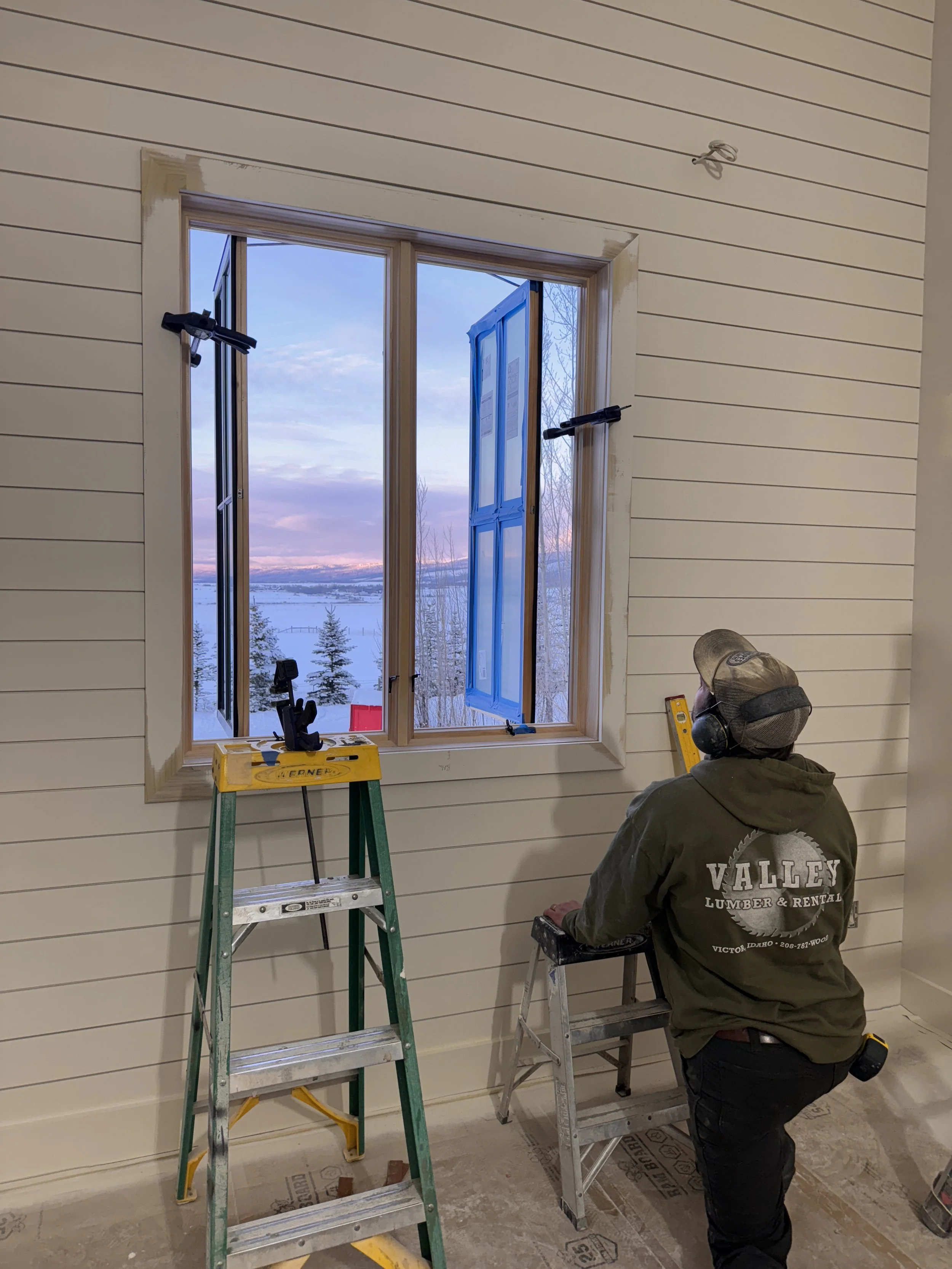 A person working on a window installation in a house, with a scenic view of snow-covered landscape and a sunset sky visible through the window.