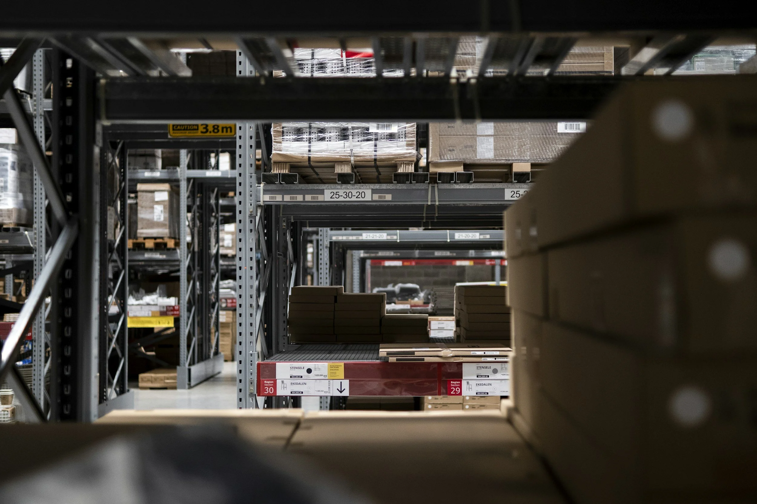 Industrial warehouse aisle with metal shelving stocked with boxes and pallets of goods.