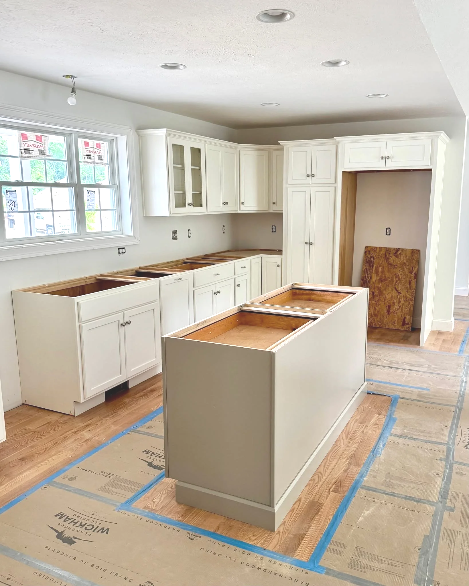 Kitchen under renovation with white cabinets, an island, and unfinished countertops, with blue painter's tape on the floor.